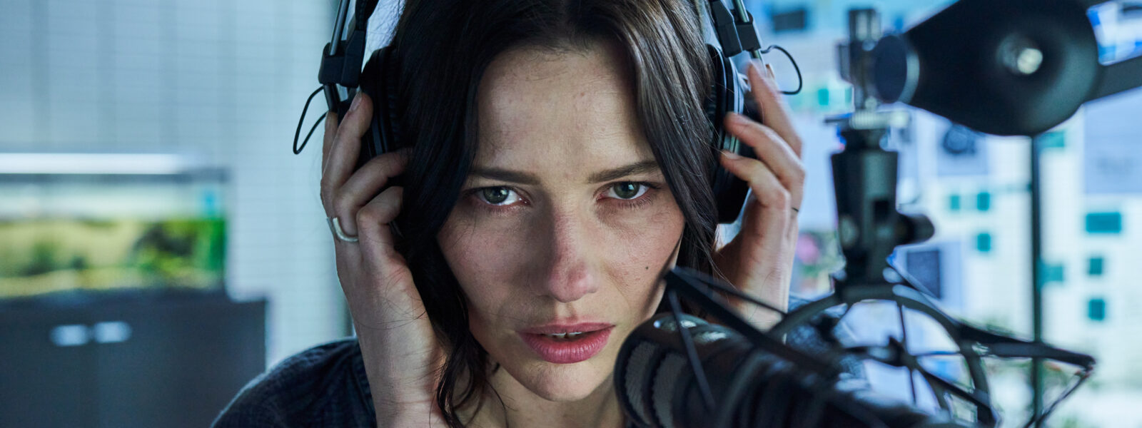 A woman wearing headphones looks worried in front of a mic