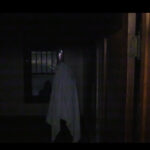 A figure stands with a white sheet over it, in the dark