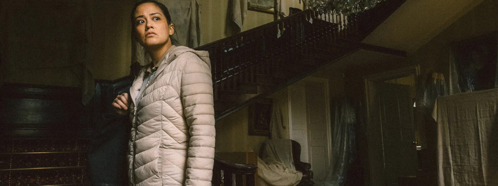 A filipino woman wearing a puffy light grey coat stands underneath a grand staircase
