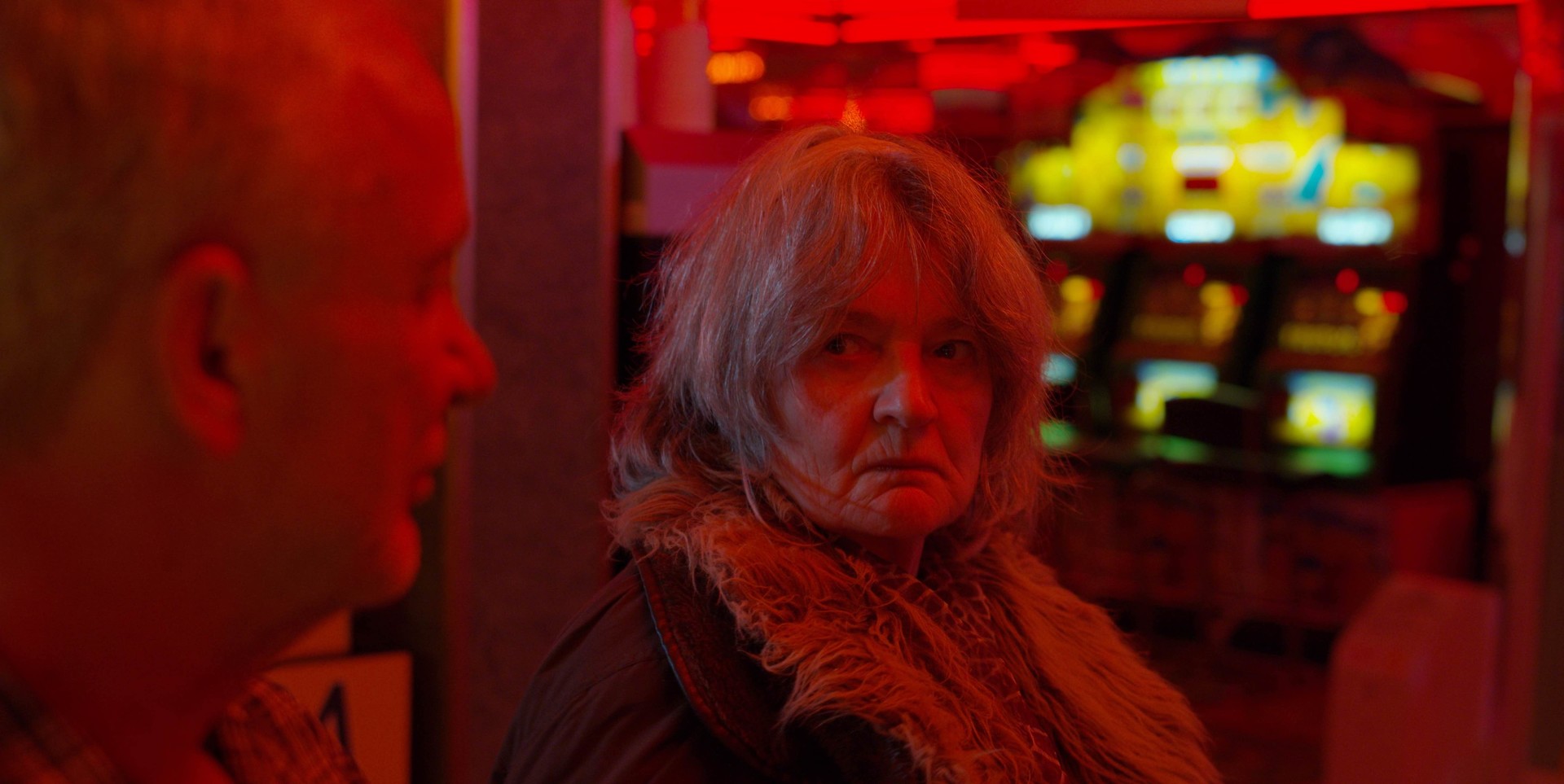 An old woman scowls at a man. They're covered in red light.