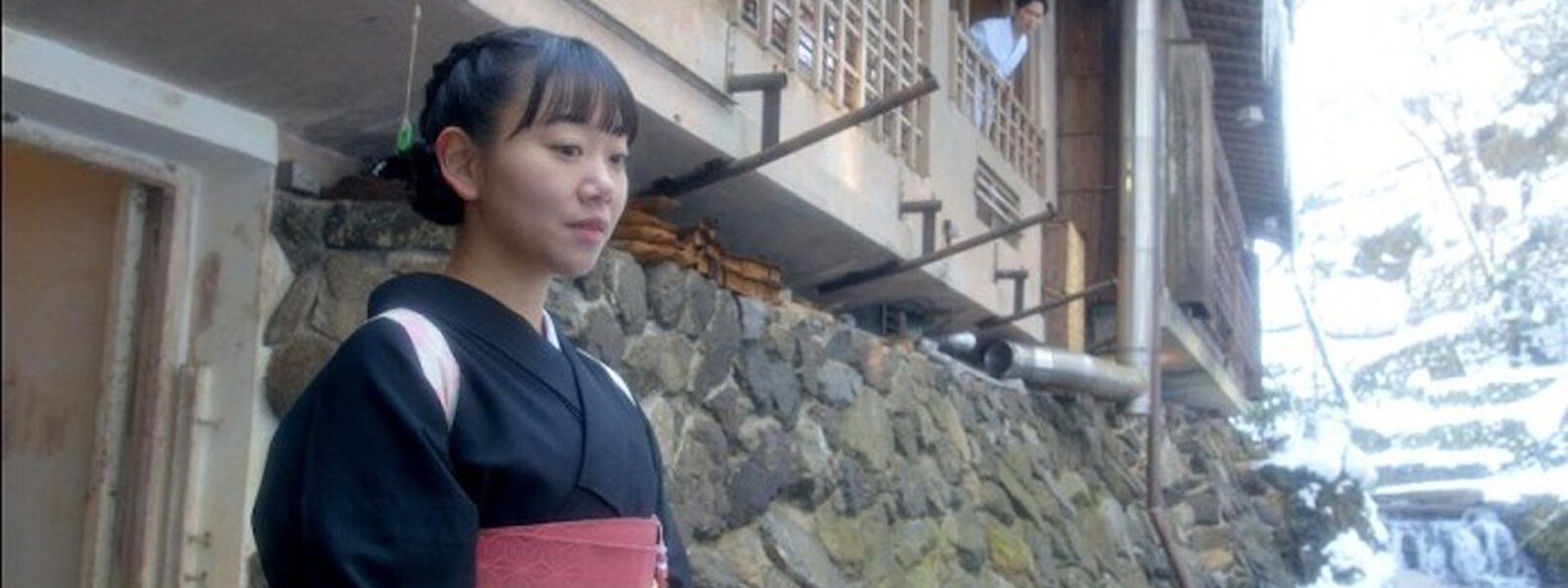 A girl in a kimono stands outside a hot springs hotel