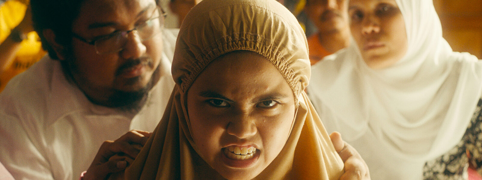 A young girl with a head covering bears her teeth