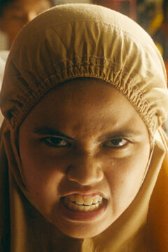 A young girl with a head covering bears her teeth