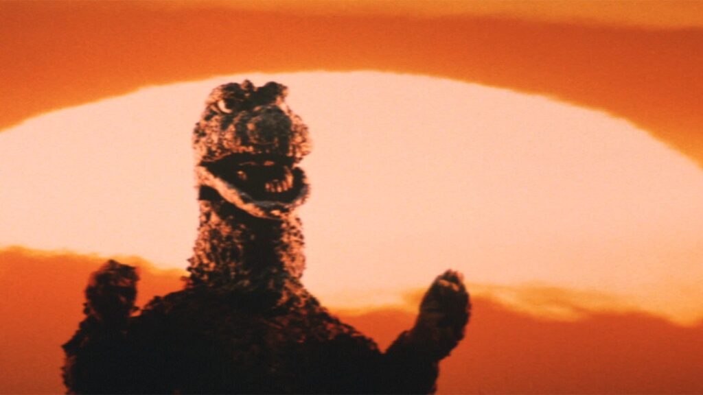 A classic view of Showa-era Godzilla, arms slightly raised and mouth open, a blazing orange sun behind him.