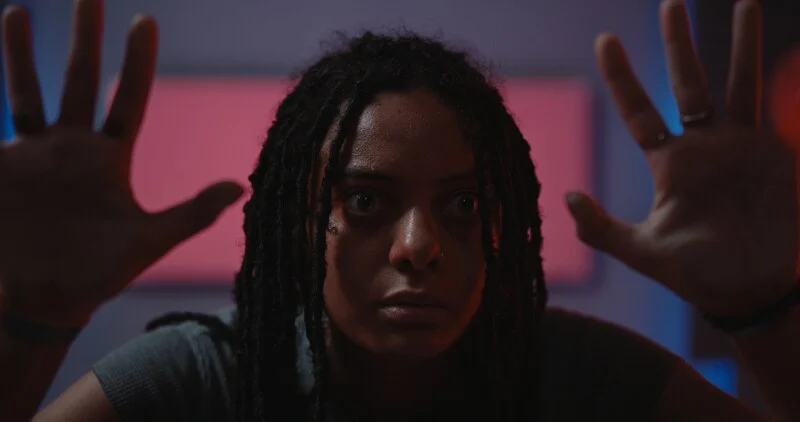 A distressed young woman with her hands up on a clear pane of glass directly in front of her.