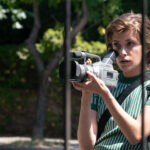 A young woman holds an large video camcorder.