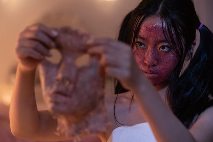 A young woman holding a face skin covered in blood