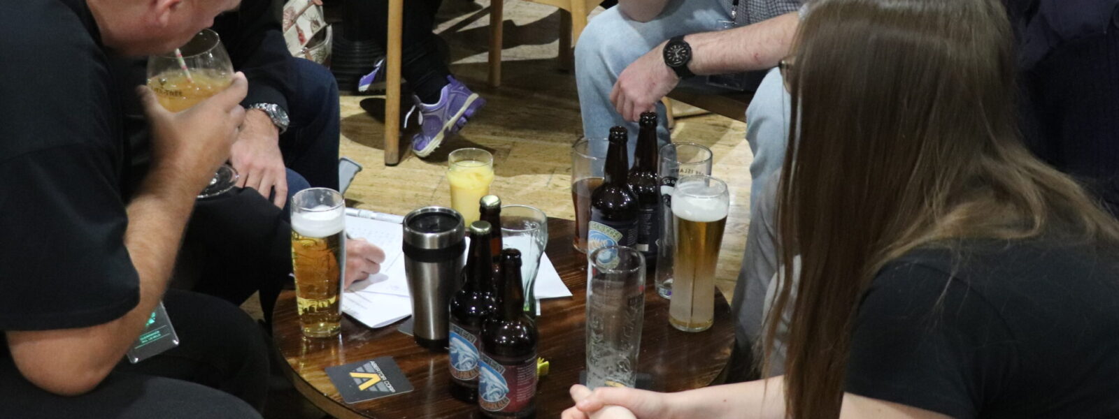 A group of people sitting around a low table, covered in bottles and glasses, ruminating over a sheet of paper.