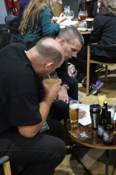 A group of people sitting around a low table, covered in bottles and glasses, ruminating over a sheet of paper.