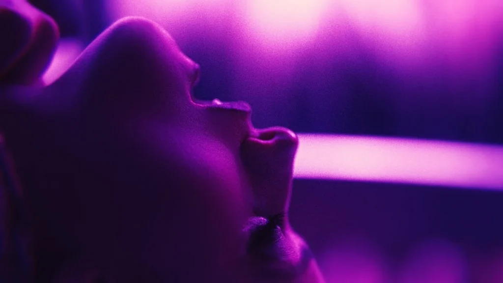 A close-up of a woman's head, thrown back in what looks to be bliss, the entire image awash in pink and purple light.