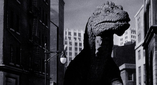 In black and white, a dinosaur-type creature standing among tall city buildings.